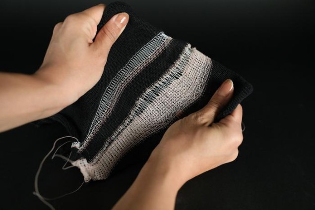 MIT Actuating Fibers Phtoto of a piece of fabric made from a liquid crystal elastomer fibre that can change its shape in response to thermal stimuli. The fabric is grey and two hands are stretching it