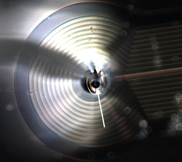 Tiny levitating particle Photo of the 48-um-diameter sphere of superconducting material, which resembles a tiny ball bearing that is levitating above a chip with wires in it